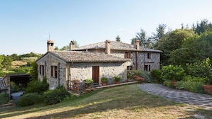 A stone house with a tiled roof, surrounded by greenery and a stone pathway.