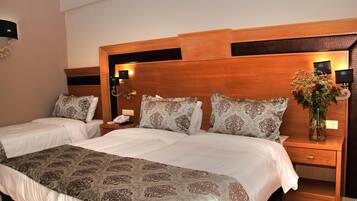 Une chambre d’hôtel avec un grand lit, deux tables de chevet, une petite table et une lampe fixée au mur.