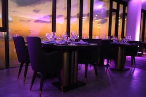 Un restaurant où les tables sont dressées pour le service, avec des chaises modernes et une vue dégagée grâce à de grandes fenêtres.