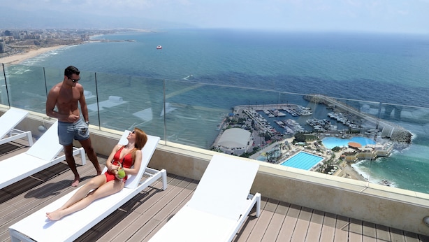 A balcony with two white lounge chairs, a pool, and a view of the ocean and marina. - Lancaster Plaza Beirut (Beirut)