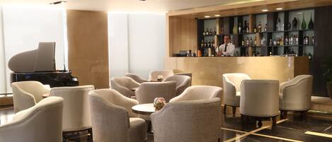 A modern lobby with a piano, comfortable seating, and a bar area with various bottles.