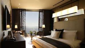 A hotel room with a large bed, a desk with a coffee maker, a chair, and a view of the ocean. - Lancaster Plaza Beirut (Beirut)