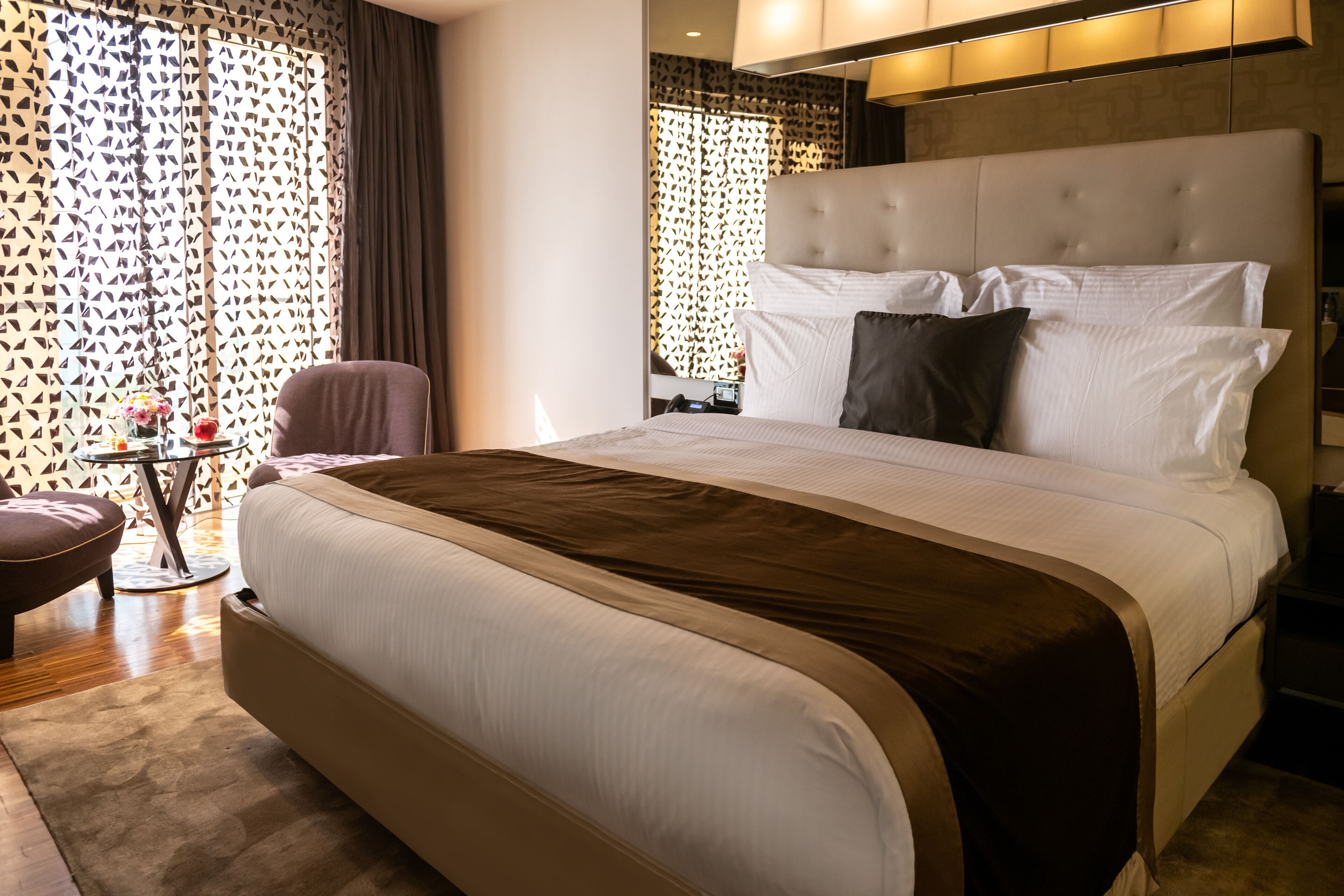 A hotel room with a large bed, a bedside table, a chair, and a decorative wall panel.