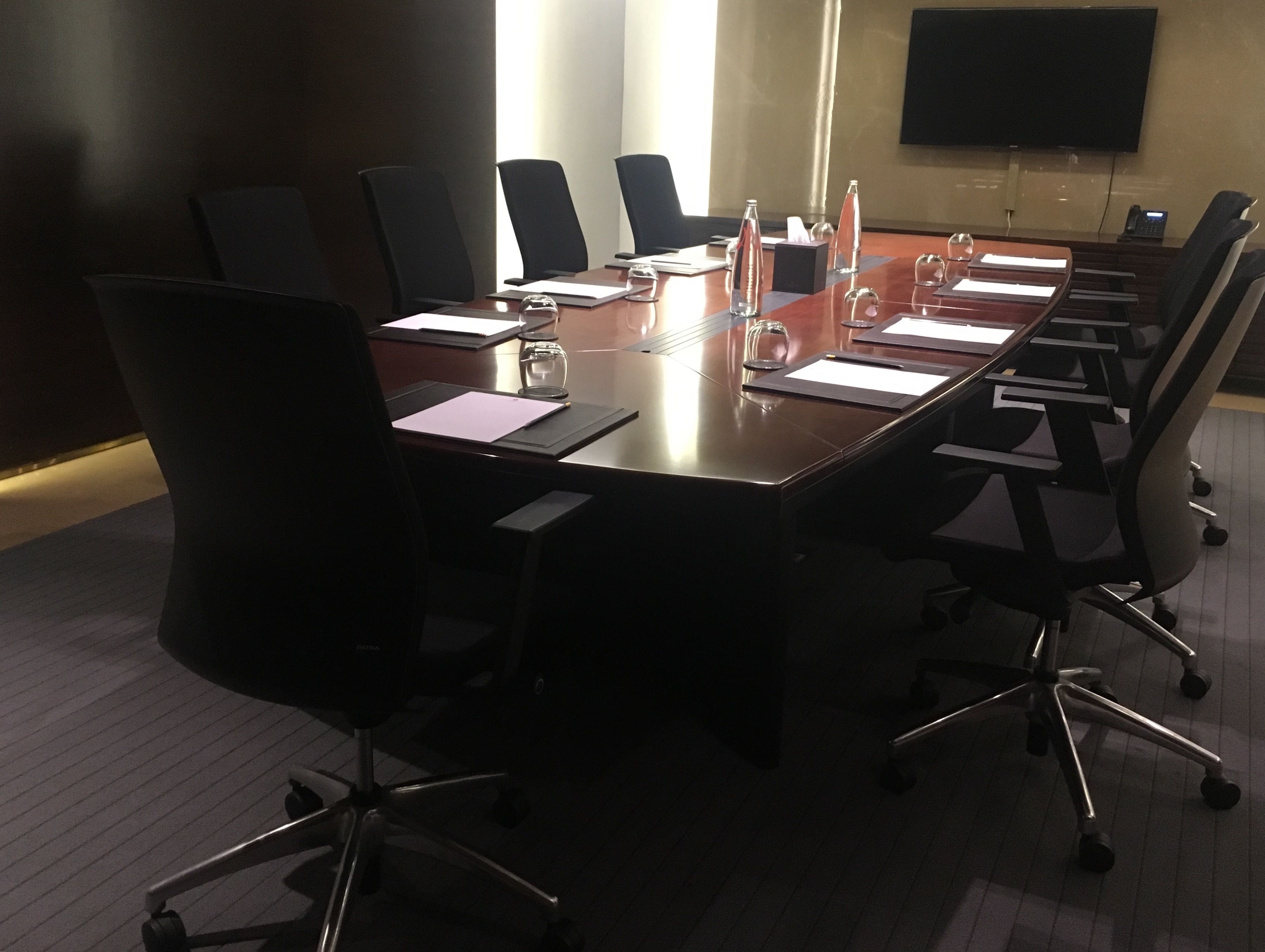 A conference room with a long table, black chairs, and a flat-screen TV on the wall.
