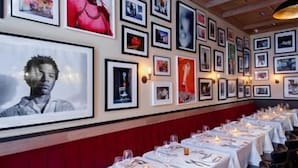 Un restaurante con largas mesas dispuestas para comer, cuadros en las paredes y una decoración en tonos rojo y blanco.