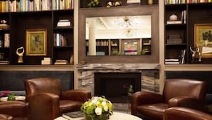 Una biblioteca con sillones de cuero, chimenea y estanterías llenas de libros y objetos decorativos.