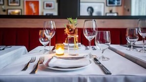Un ambiente de restaurante con una mesa preparada para dos, con copas de vino, cubiertos y una vela.