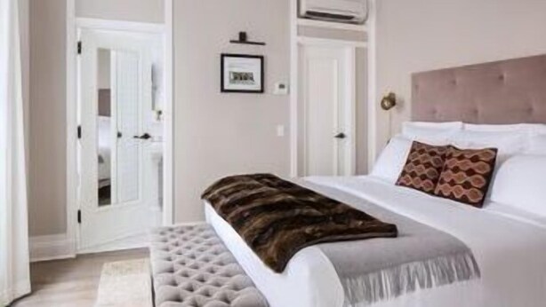 Un dormitorio con cama, una banca, un cuadro enmarcado en la pared y un equipo de aire acondicionado.