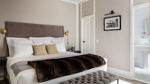 Un dormitorio con cama, mesitas de noche, lámpara, un cuadro enmarcado en la pared y una puerta.