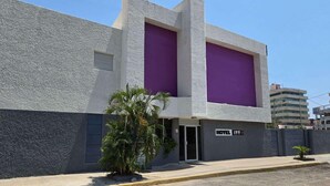 Un bâtiment moderne avec une façade grise à texture, une entrée violette et une enseigne indiquant qu’il s’agit d’un hôtel.