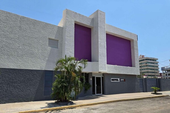A modern building with a grey textured facade, a purple entrance, and a sign indicating it is a hotel. - Hotel Itto (Acapulco)