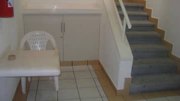 A corner of a room with a white chair, a small table, a cabinet, and a staircase with a handrail.