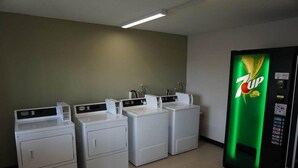 Ein Waschraum mit vier Waschmaschinen und einer 7UP-Getränkeautomat.