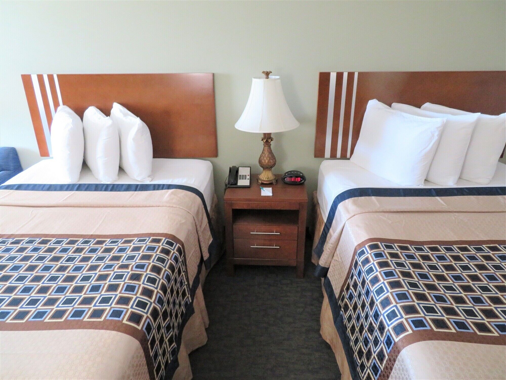 A hotel room with two beds, each with a headboard, a bedside table with a lamp, and a clock.