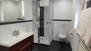 Un baño moderno con ducha envuelta en vidrio, inodoro blanco y tocador con espejo.