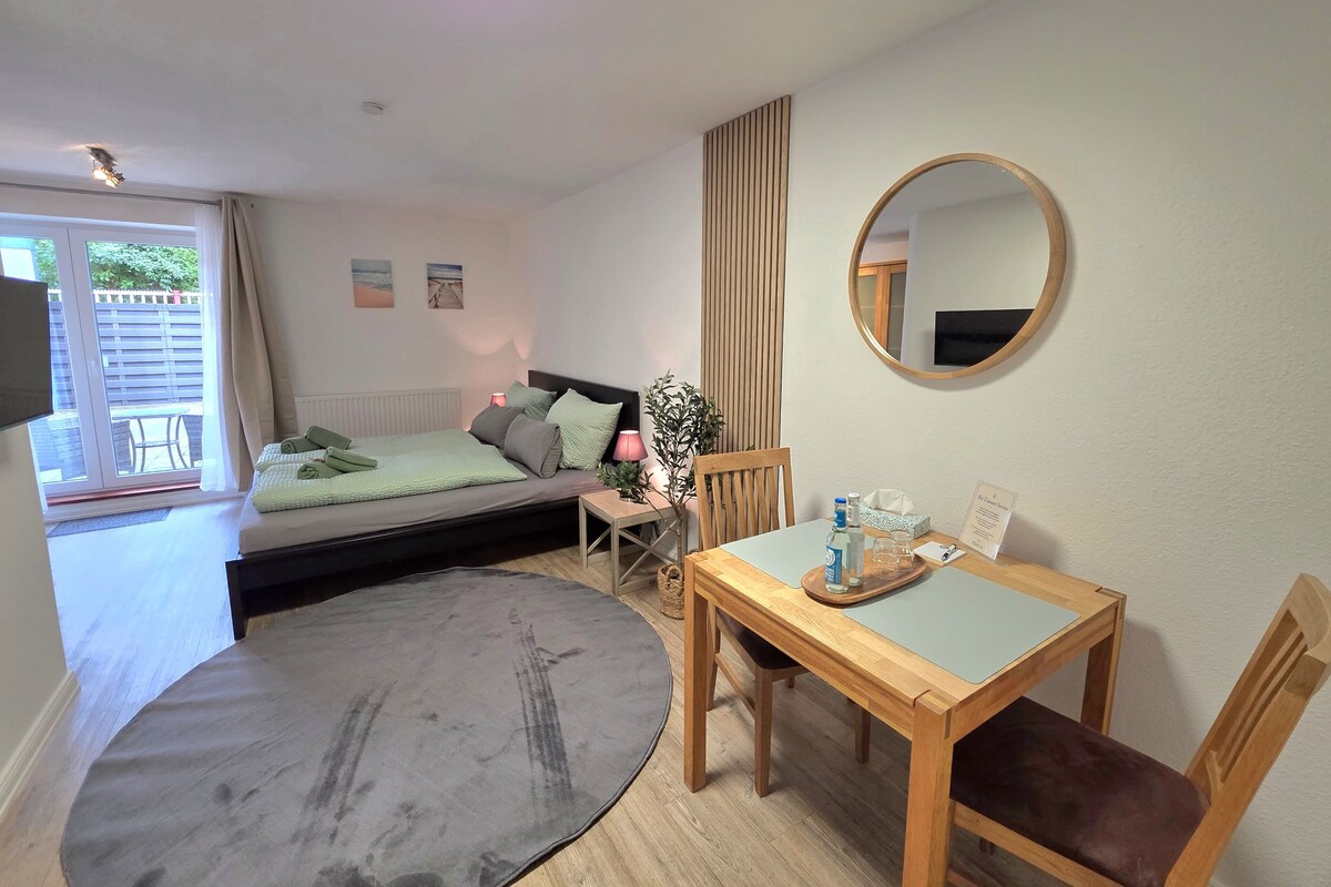 A bedroom with a bed, bedside table, chair, and a small table with a mirror.