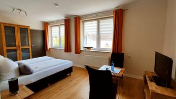 Quarto de hotel com cama, escrivaninha, cadeira, televisão e janela com cortinas.