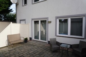 A patio area with a white fence, two wicker chairs, a small table, and a potted plant.