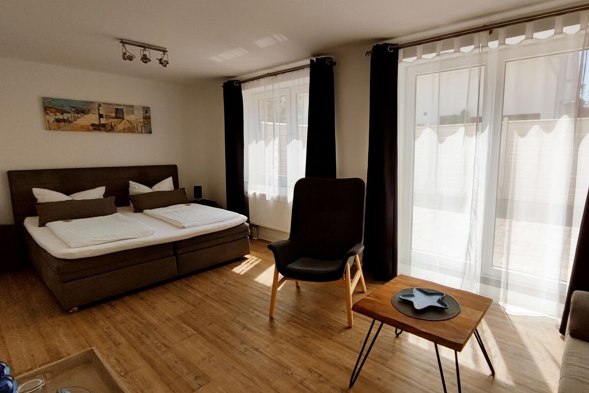 Een hotelkamer met een bed, een stoel, een klein tafeltje en grote ramen met gordijnen.