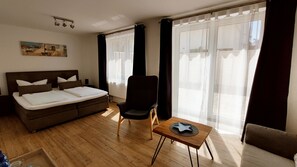 Een hotelkamer met een bed, een stoel, een klein tafeltje en grote ramen met gordijnen.