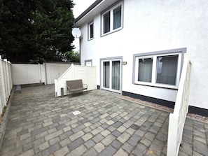 A residential building with a paved patio, a bench, and a white fence.