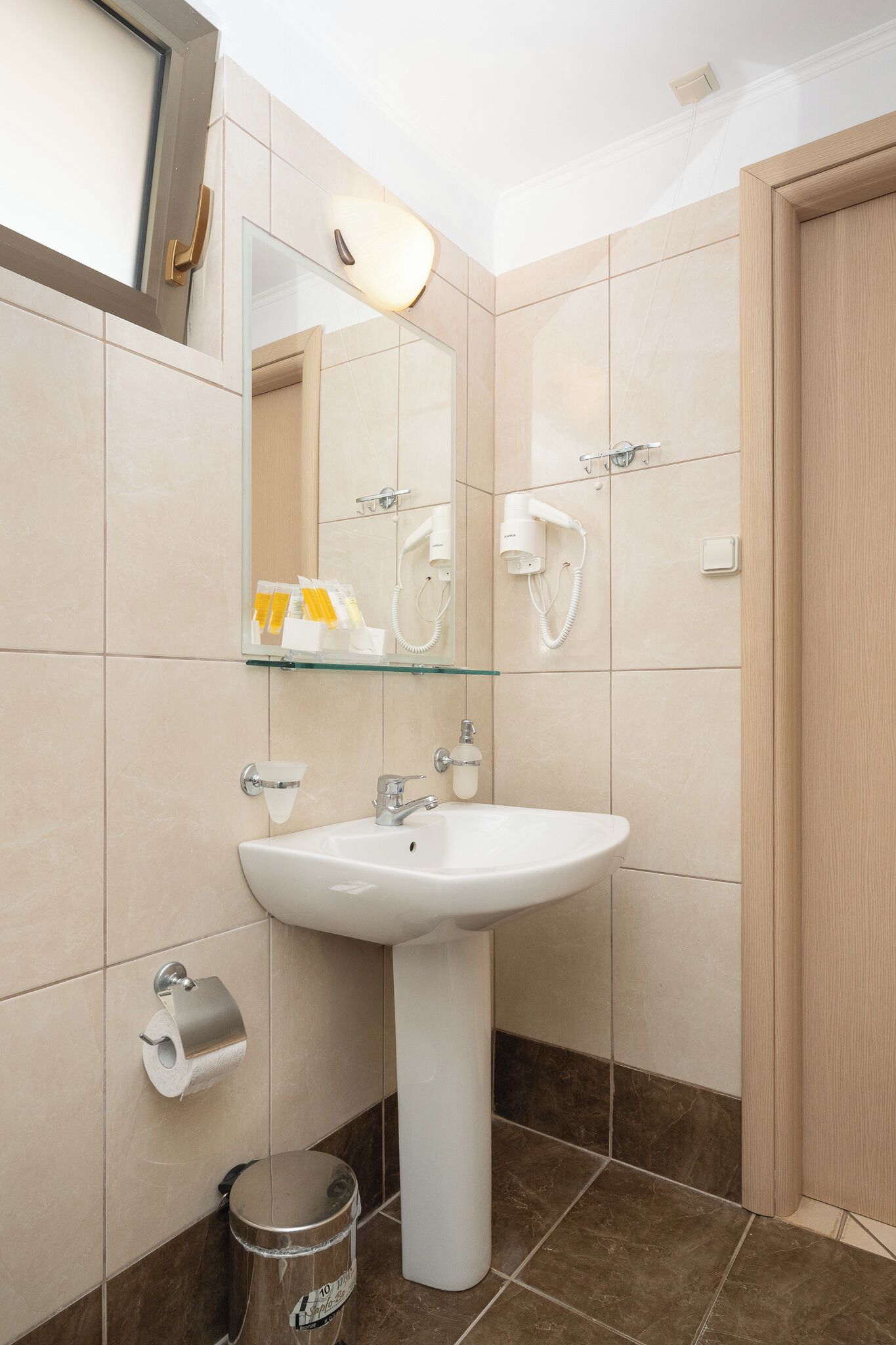 A bathroom with a pedestal sink, a mirror, a hairdryer, and a trash can.