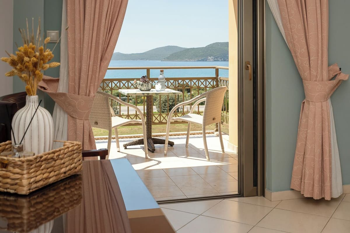 A room with a view of the sea, a balcony with chairs, and a table with a vase and basket.