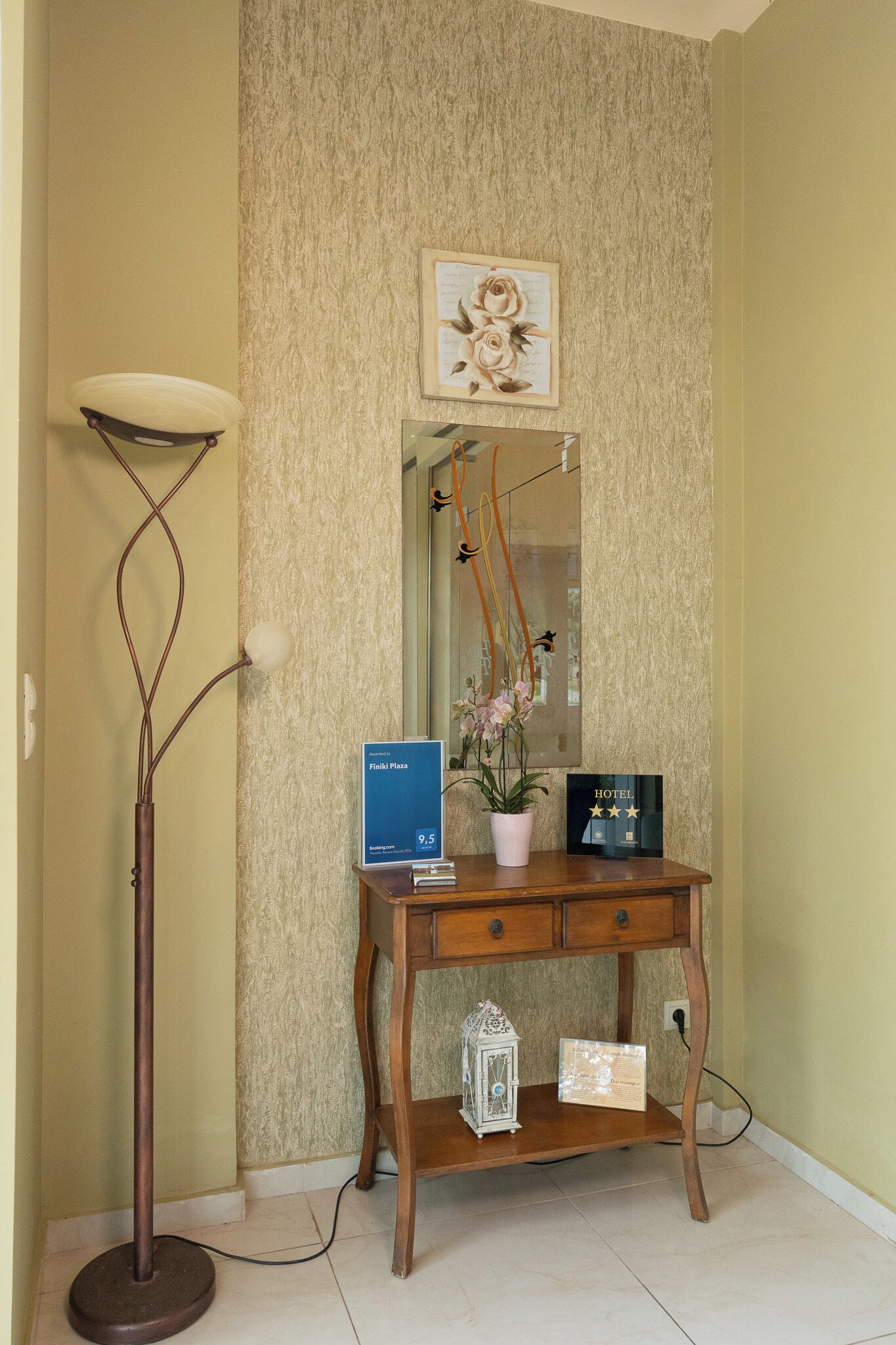 Een hotel receptiebalie met een lijstwerk met bloemen, een potplant, een bord en een decoratieve lantaarn.