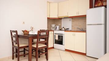 A compact kitchen with a dining table, chairs, a coffee maker, an oven, and a refrigerator.