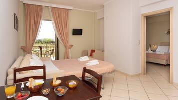 A hotel room with a dining area, a bed, a TV, and a balcony with curtains.