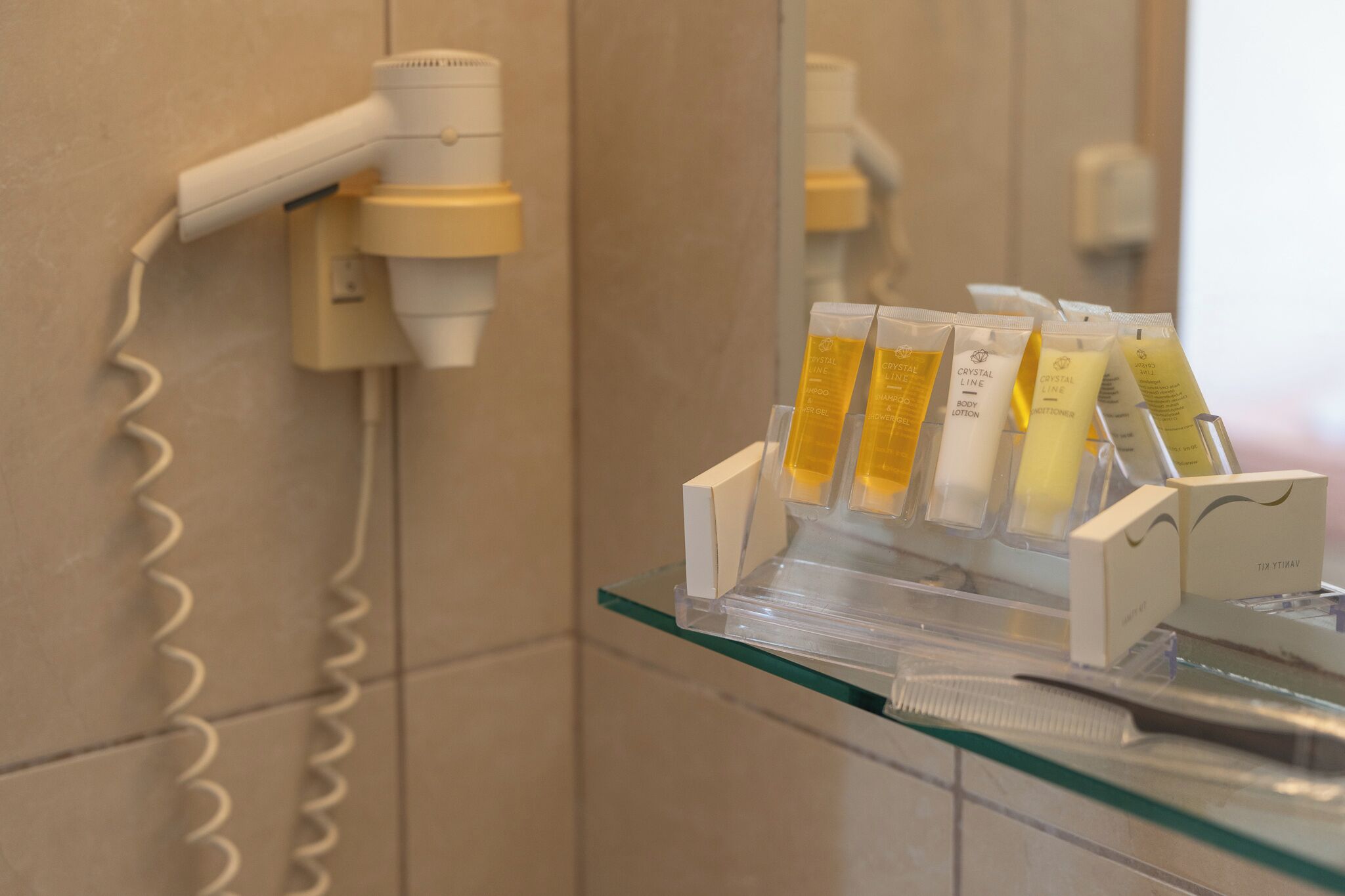 Un baño con secador de pelo, un estante de vidrio con artículos de tocador y un espejo.