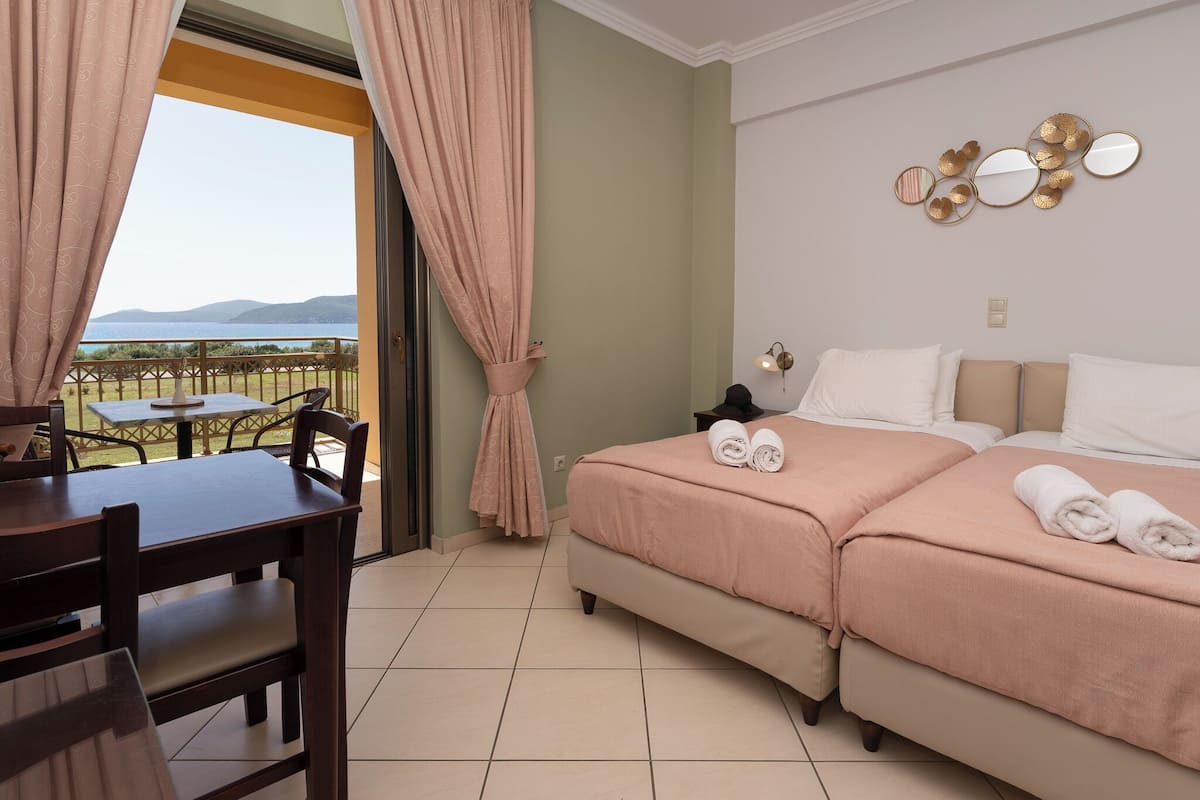 A hotel room with a balcony, a bed with pink bedding, a table with chairs, and a wall with decorative mirrors.