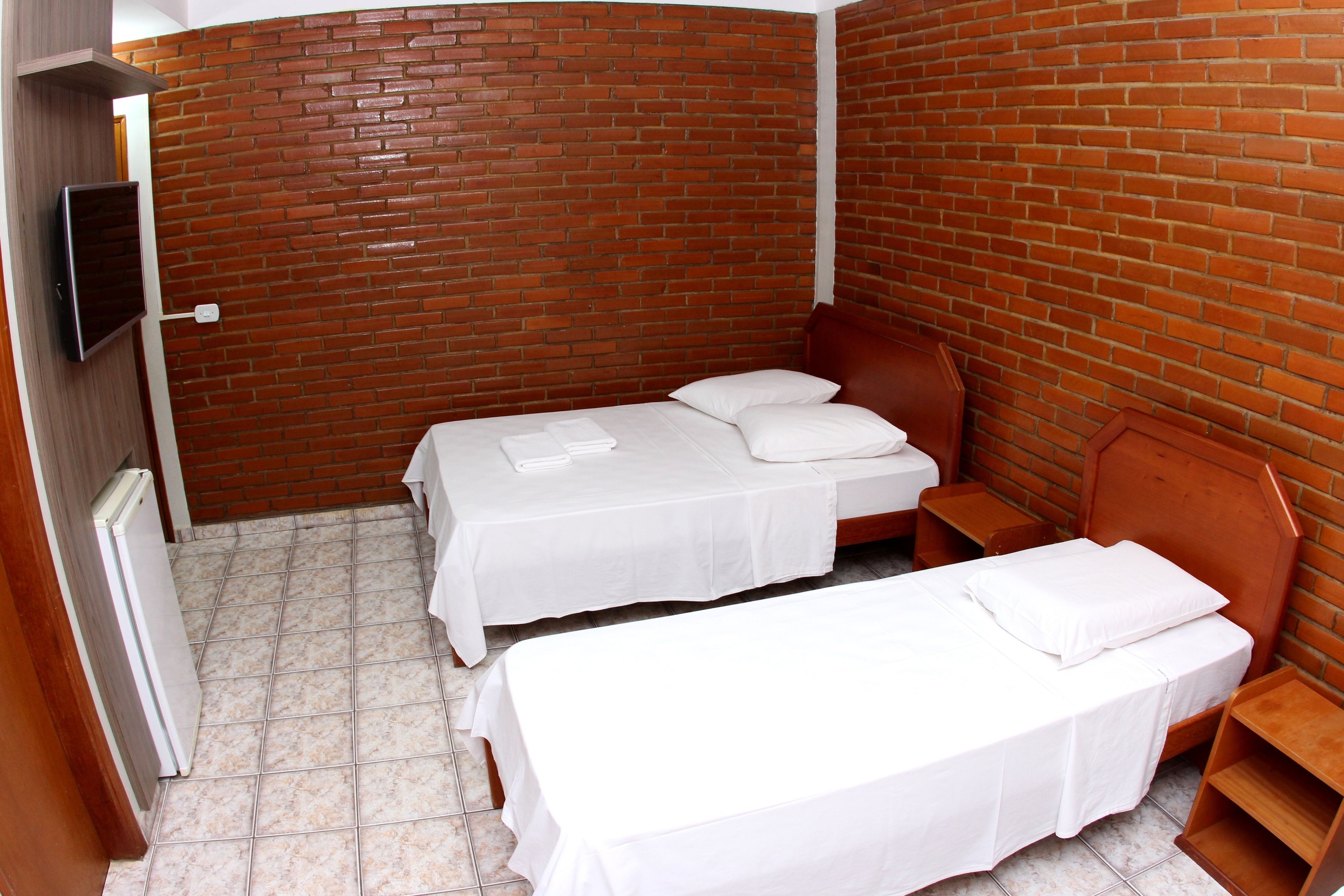 Una habitación pequeña y privada con dos camas individuales, un cabecero de madera y suelo de baldosas.