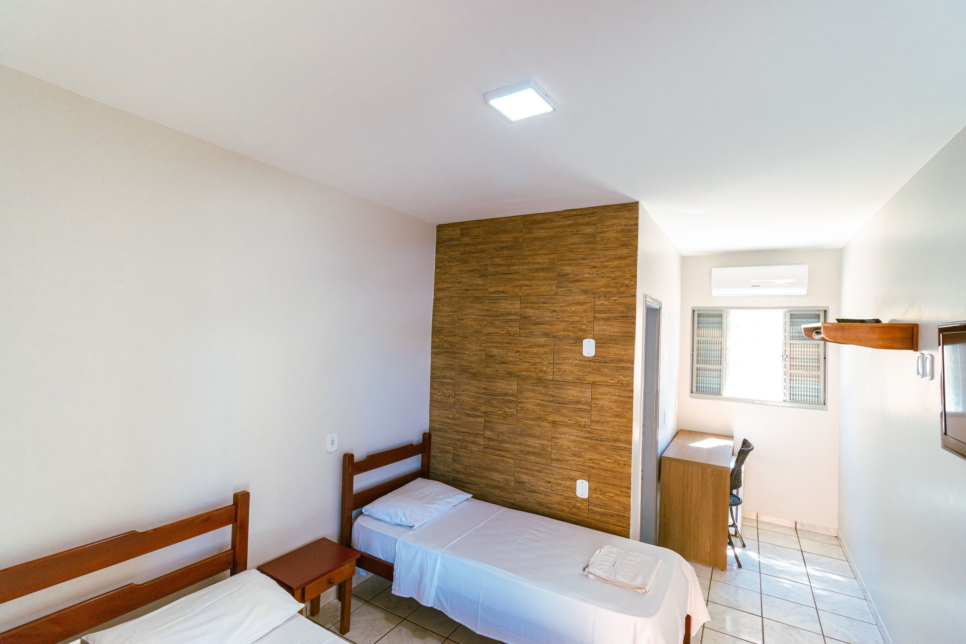 A small, well-lit room with a wooden headboard bed, a wooden desk, and a small table.
