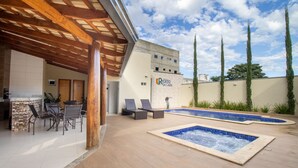 Zona de piscina exterior con sillones de descanso, una zona de estar cubierta y un edificio con un letrero que dice 