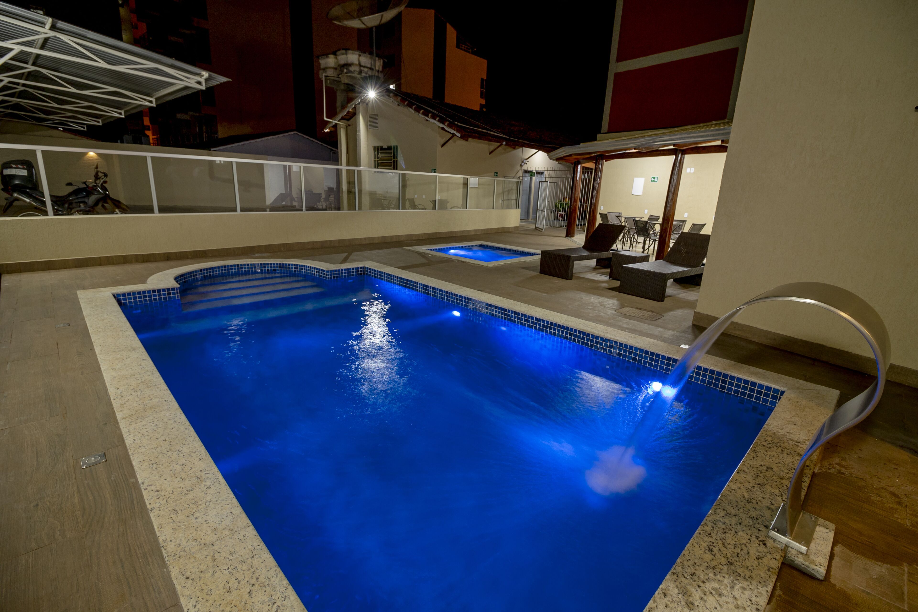 Une piscine intérieure dotée d’un élément décoratif à l’eau claire, d’un espace salon aménagé en contrebas et d’un patio couvert avec des sièges d’extérieur.