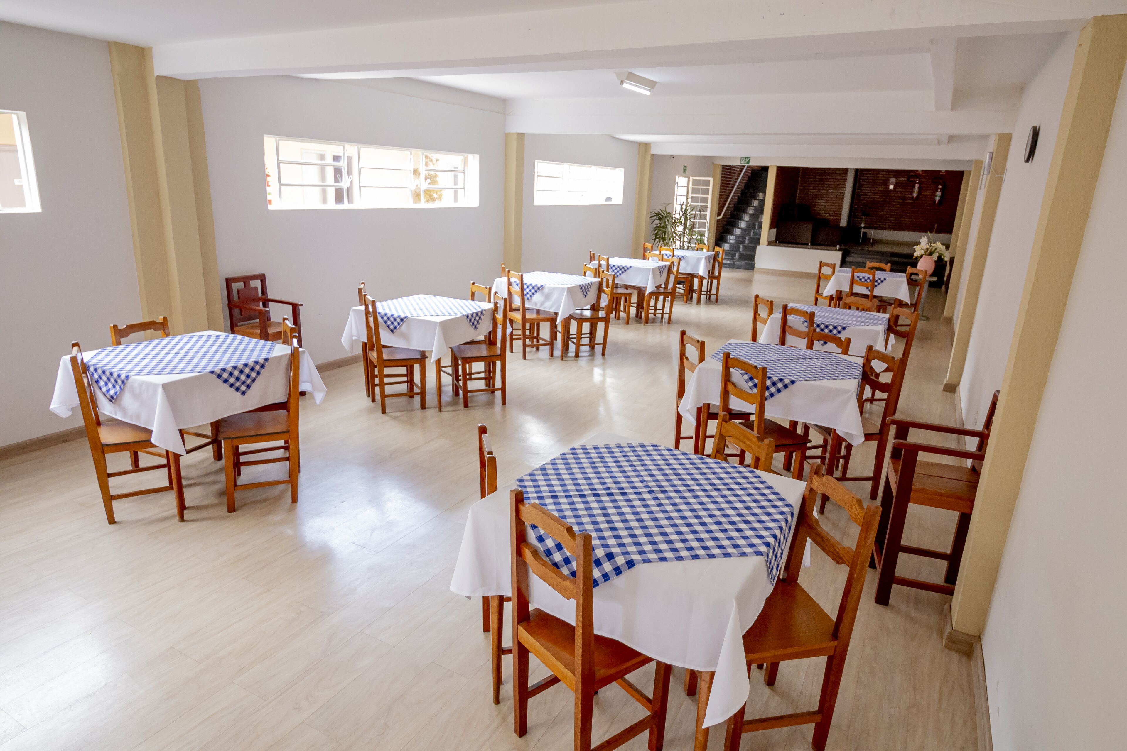 Comedor con varias mesas y sillas, dispuesto en un espacio amplio con luz natural proveniente de ventanas.