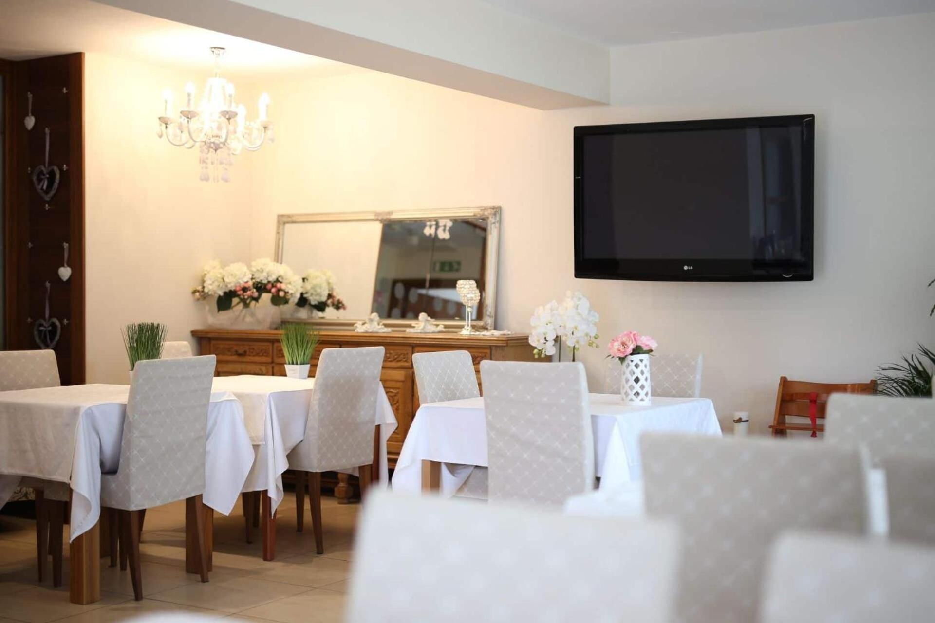 A dining area with multiple tables and chairs, a chandelier, a flat-screen TV, and a mirror on the wall.