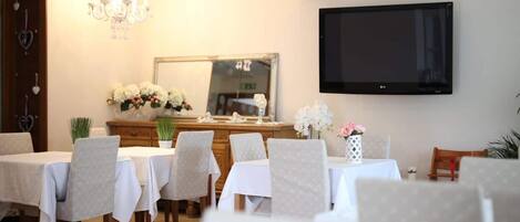 A dining area with multiple tables and chairs, a chandelier, a flat-screen TV, and a mirror on the wall.