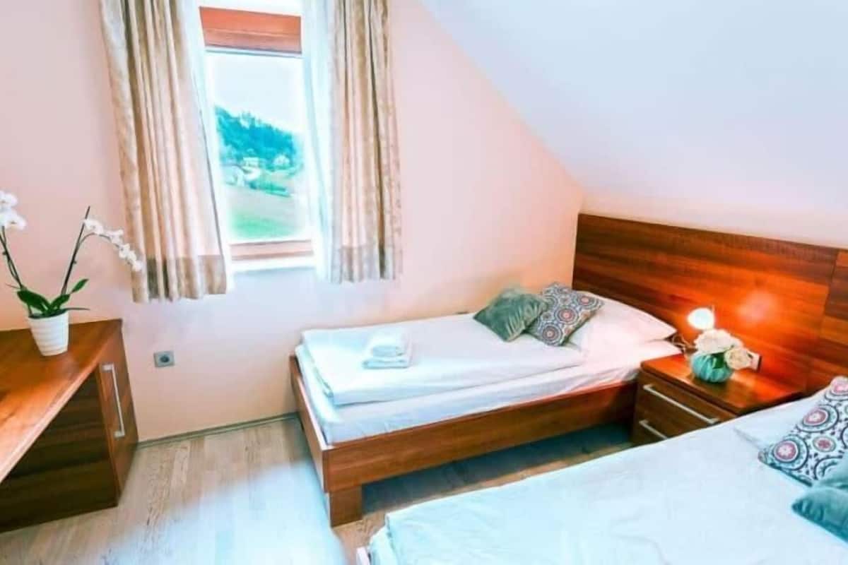 Une chambre à coucher avec deux lits, une tête de lit en bois, une table de chevet avec une lampe et une fenêtre avec des rideaux.
