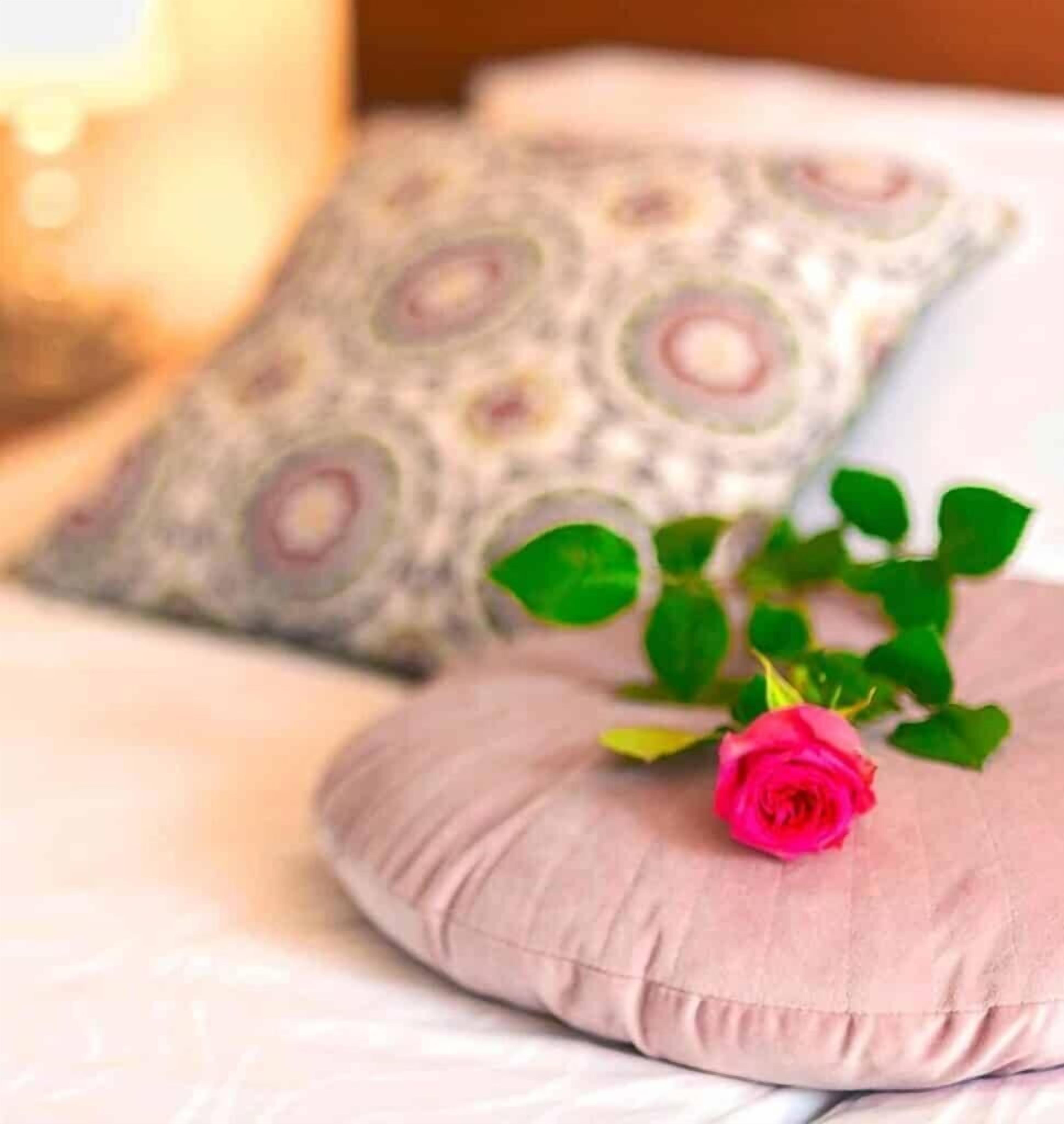 A bed with a pink pillow and a rose.