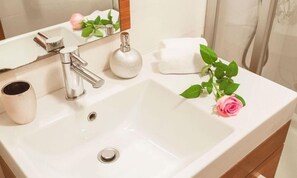 Une salle de bain avec un lavabo blanc, un miroir, une serviette, une tasse et une rose.