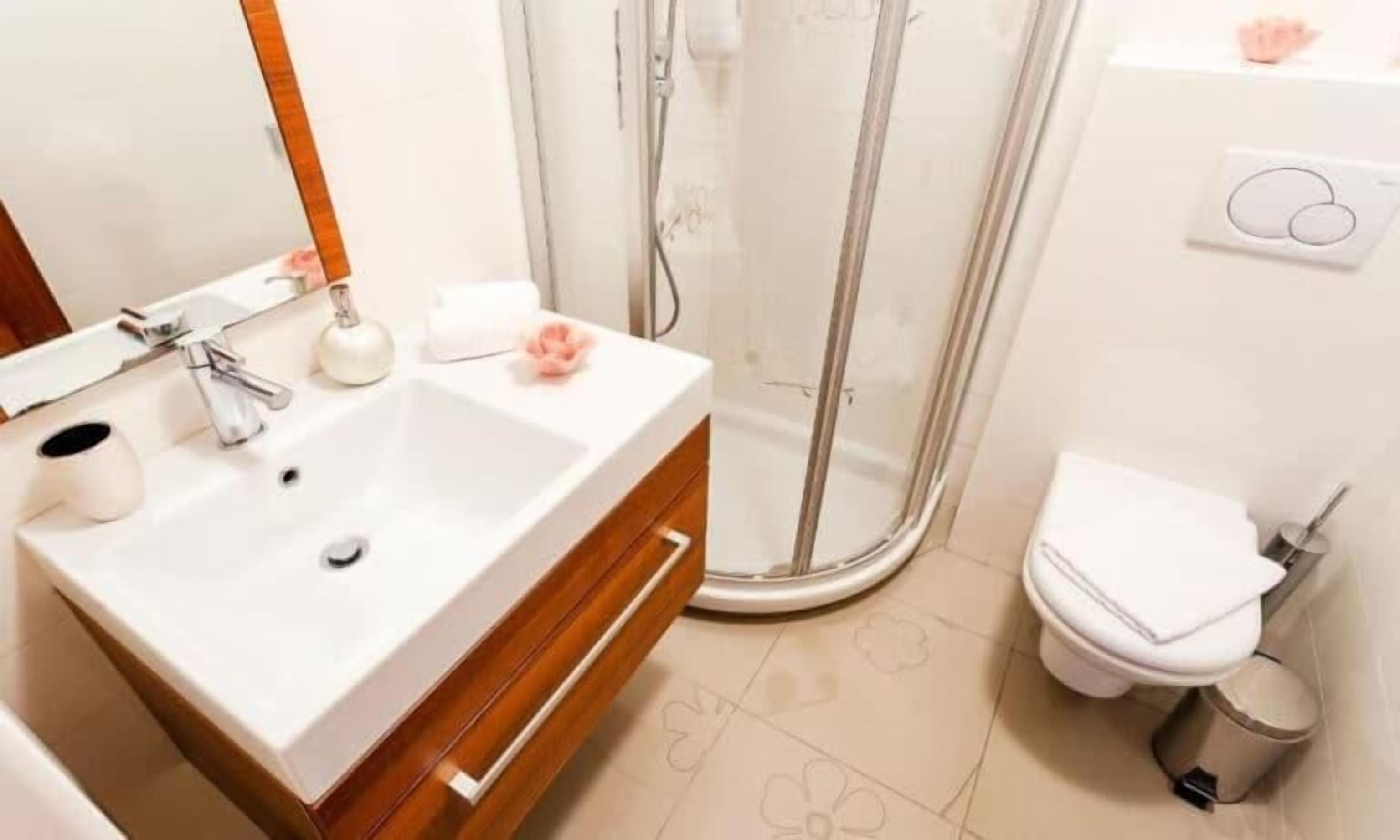 Un baño con lavamanos blanco, tocador de madera, espejo, zona de ducha y retrete.
