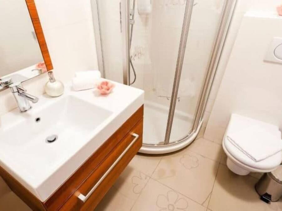 A bathroom with a white sink, wooden vanity, a mirror, a shower area, and a toilet.