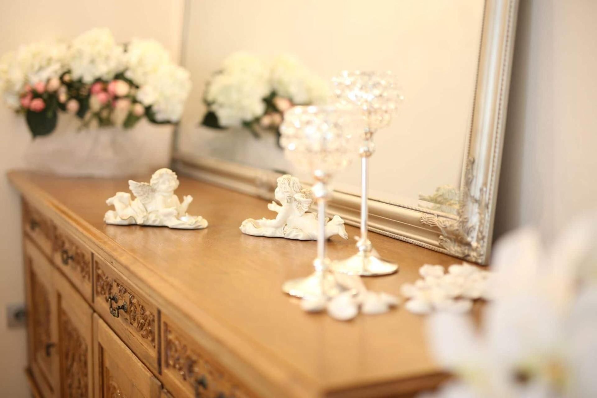 Un aparador de madera con figuritas de ángeles decorativos y un espejo que refleja un ramo de flores.