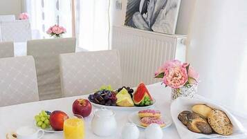 Una mesa de desayuno con frutas, pan y huevos, con un cuadro y flores al fondo.