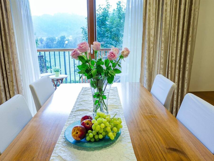 A dining table with a vase of roses and a plate of fruit.