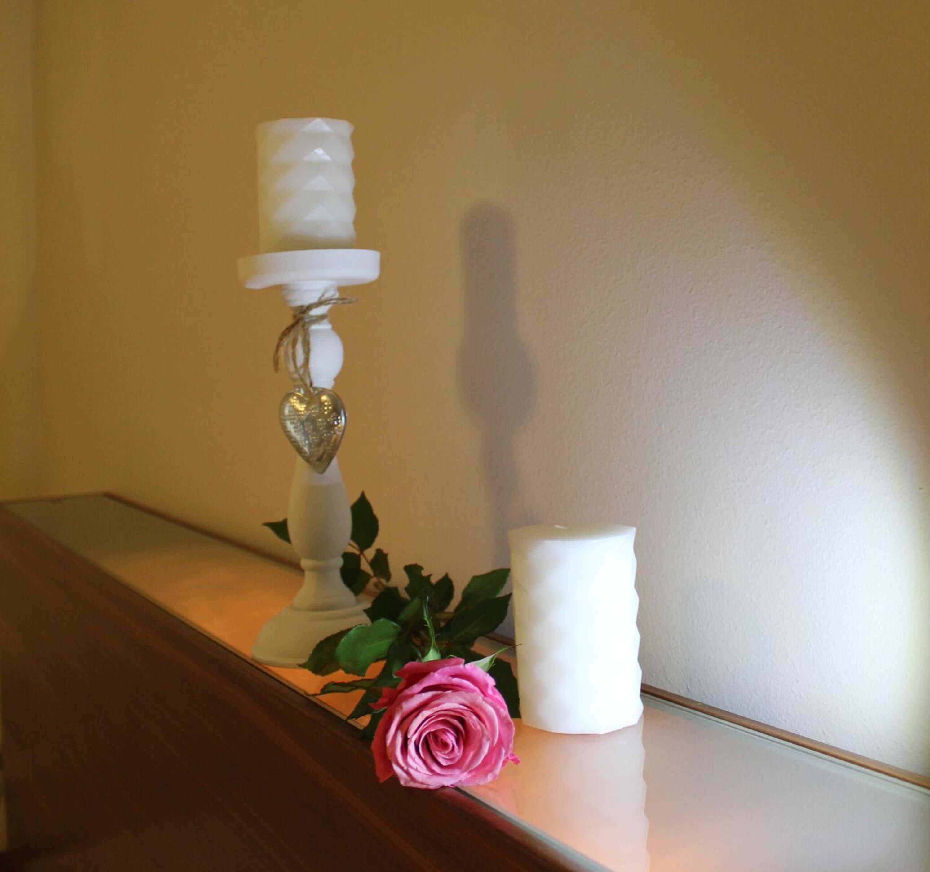 Un candelabro blanco con un adorno en forma de corazón y una rosa rosa sobre una superficie de madera.