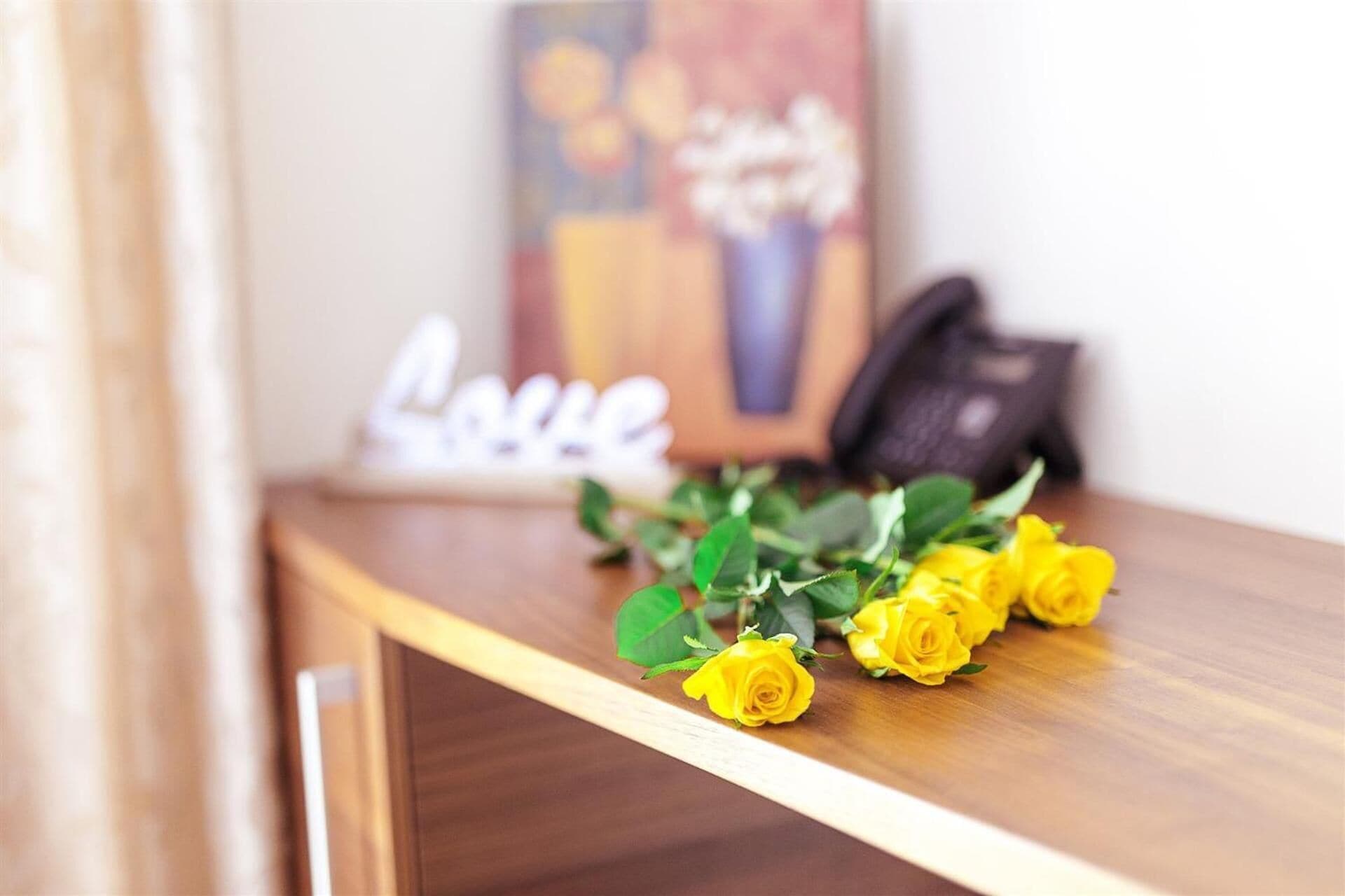 Une étagère en bois ornée d’un bouquet de roses jaunes et d’une plaque décorative sur laquelle est inscrit le mot « Amour ».
