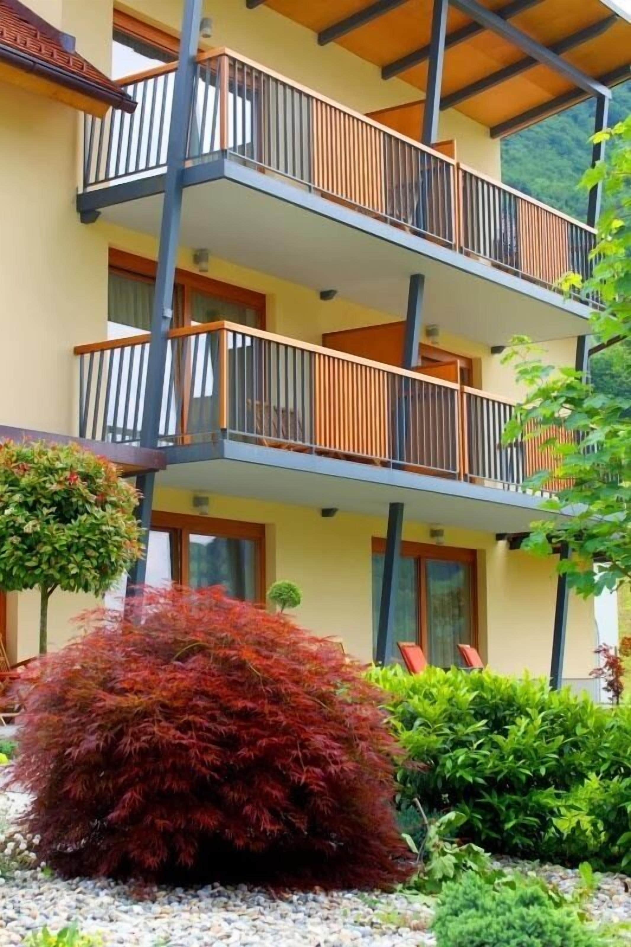 A multi-story building with balconies, a garden with red foliage, and a clear view of the surrounding landscape.